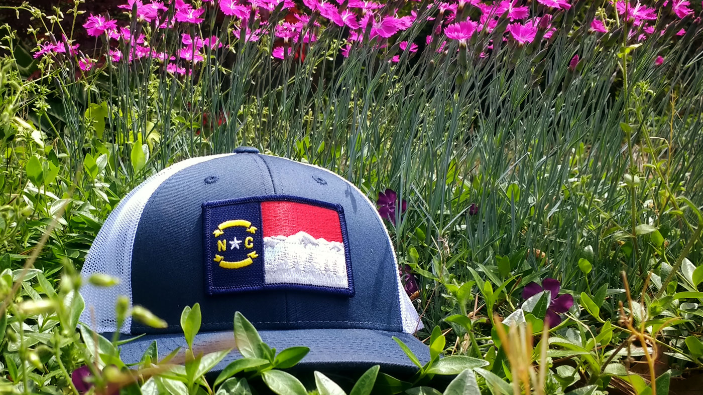 State of North Carolina outdoorsy cap in a flower field 
