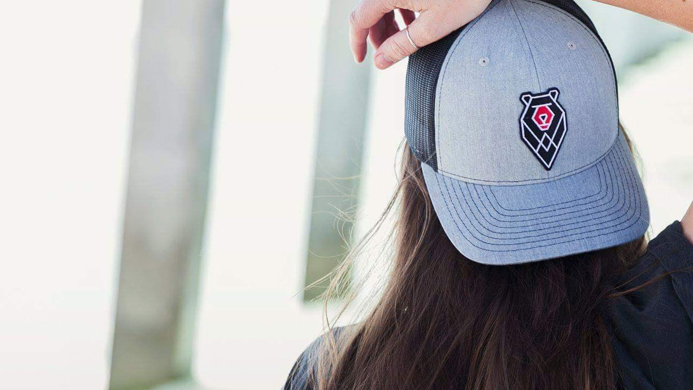 woman with long brown hair wearing bear logo hat on a breezy day 