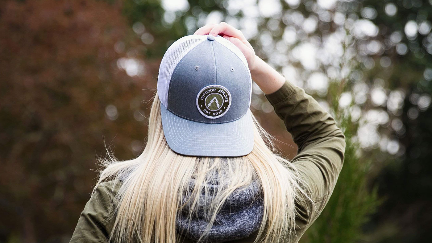Woman with blonde hair on a hike wearing a trucker patch hat