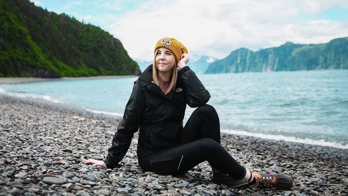 Woman in hiking clothes at rocky Alaskan shore of Upper Tazimina
